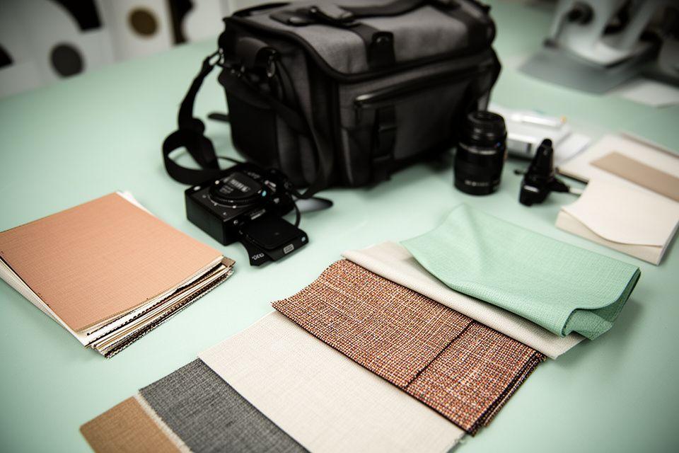 Camera bag, textile samples, and a notebook arranged on a studio table beside softly lit fabric swatches